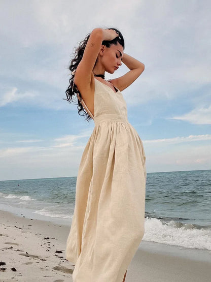 Woman in a beige dress standing on a beach with ocean waves in the background