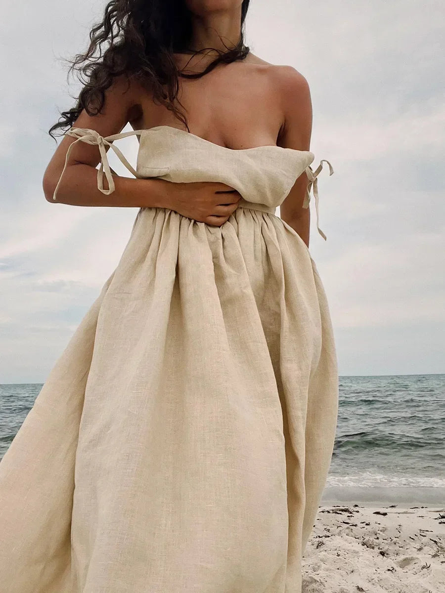 Woman wearing a beige off-shoulder dress on a beach with ocean view
