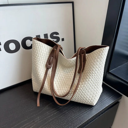White textured handbag with brown handles on a dark surface.
